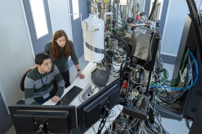 Two researchers are working with a large, complex piece of scientific equipment