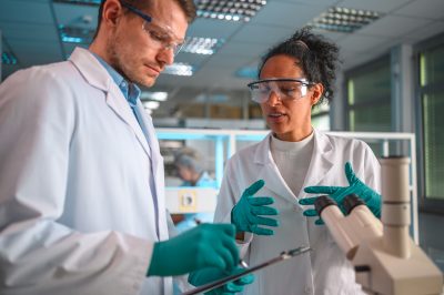 a mid-adult female and male researcher or student in a laboratory environment, engaged in a detailed discussion while reviewing test results on a clipboard.