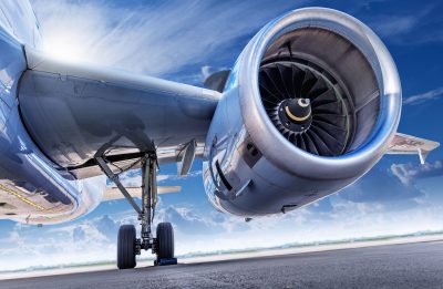 A close-up view of the landing gear and powerful jet engine of an airplane, with the large turbine blades of the engine prominently visible.